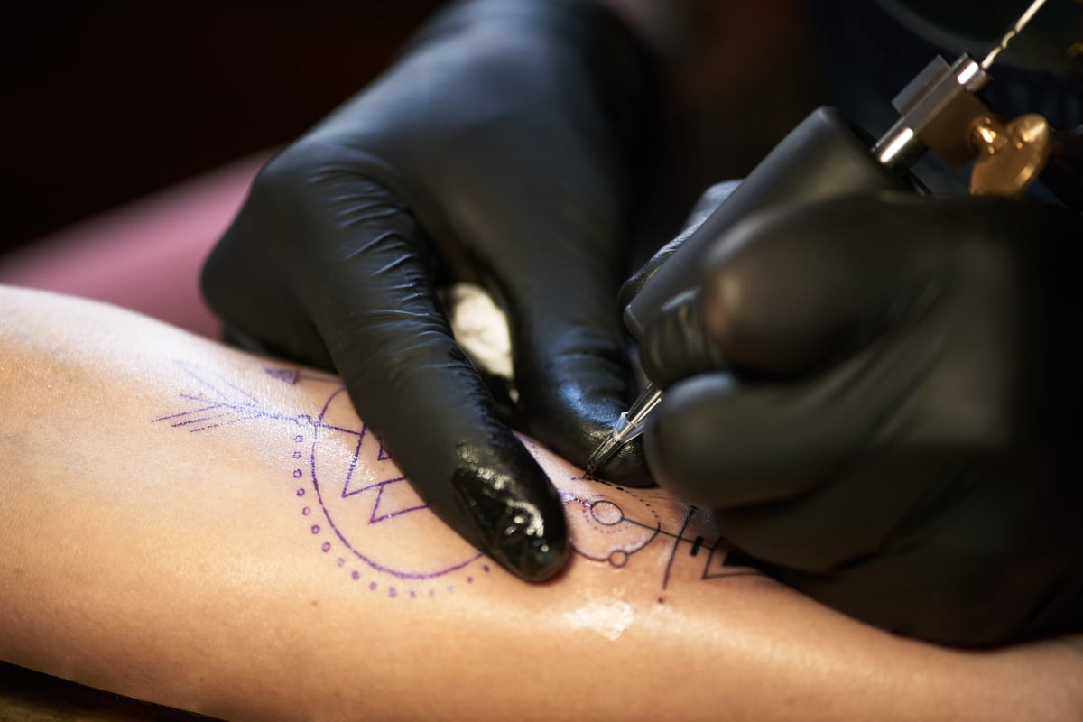 Close-up view of unrecognizable tattooist in rubber gloves drawing a tattoo with electric tattoo gun